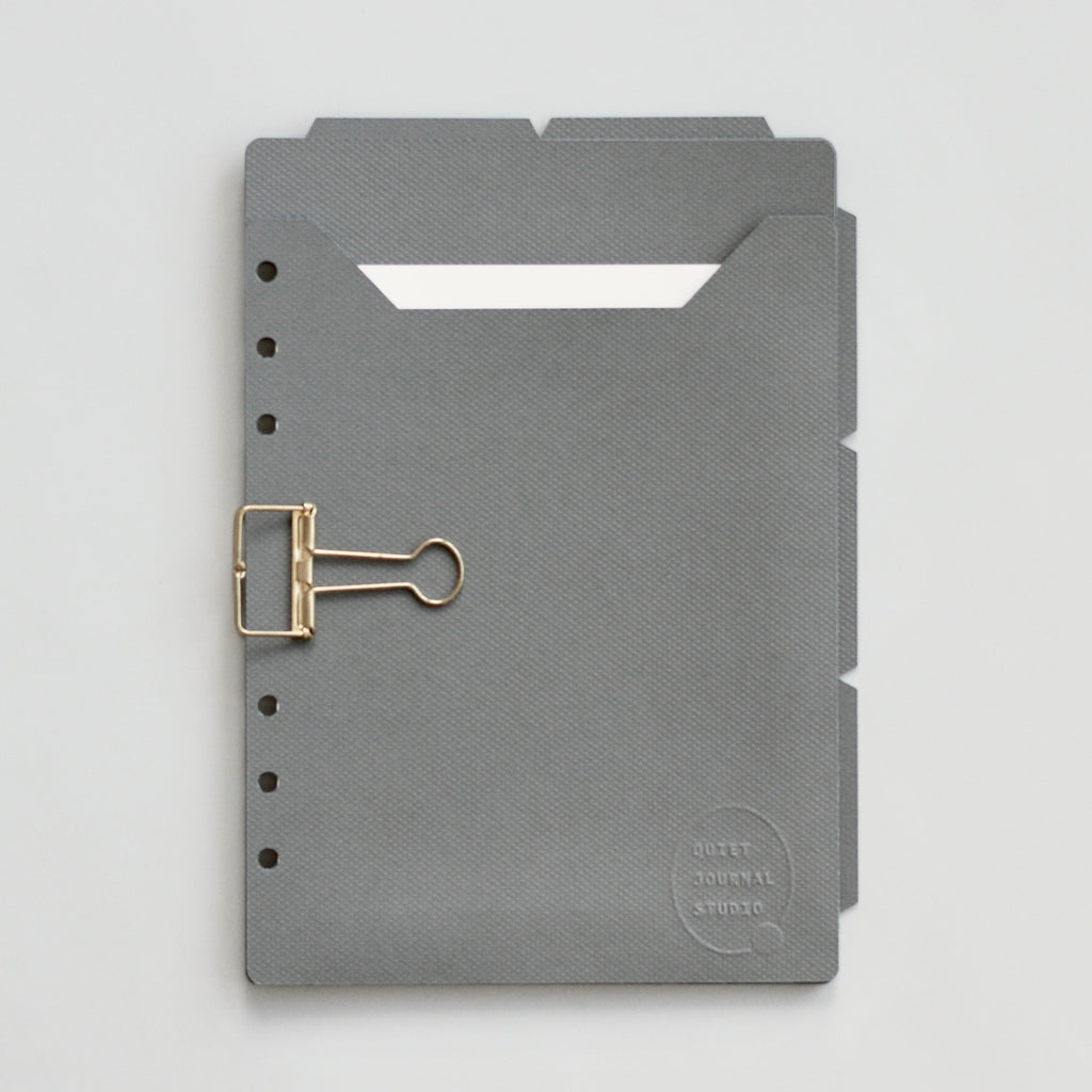 Dark gray planner dividers with a gold clip on a gray background