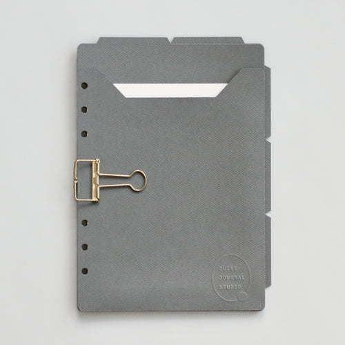 Dark gray planner dividers with a gold clip on a gray background