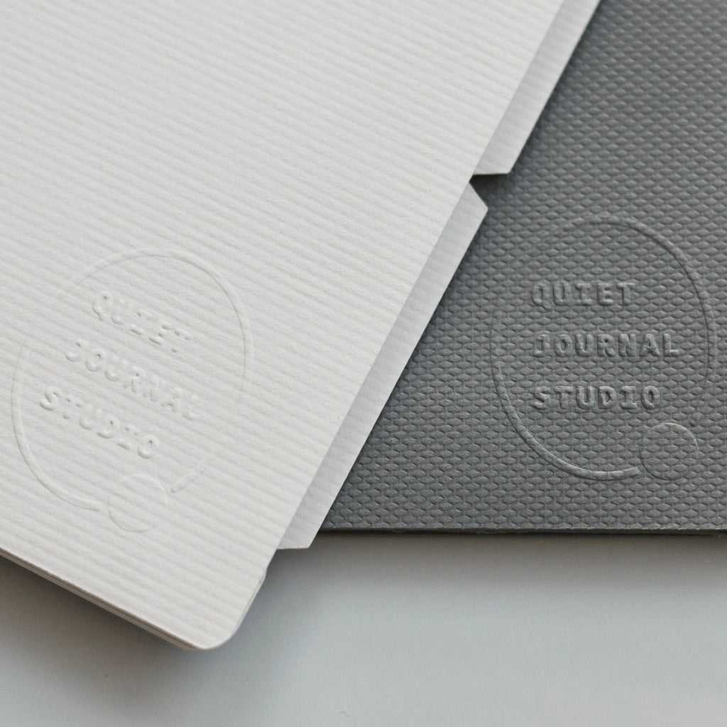Two dividers, one light gray and one dark gray, with 'Quiet Journal Studio' embossed on them, on a light gray background.