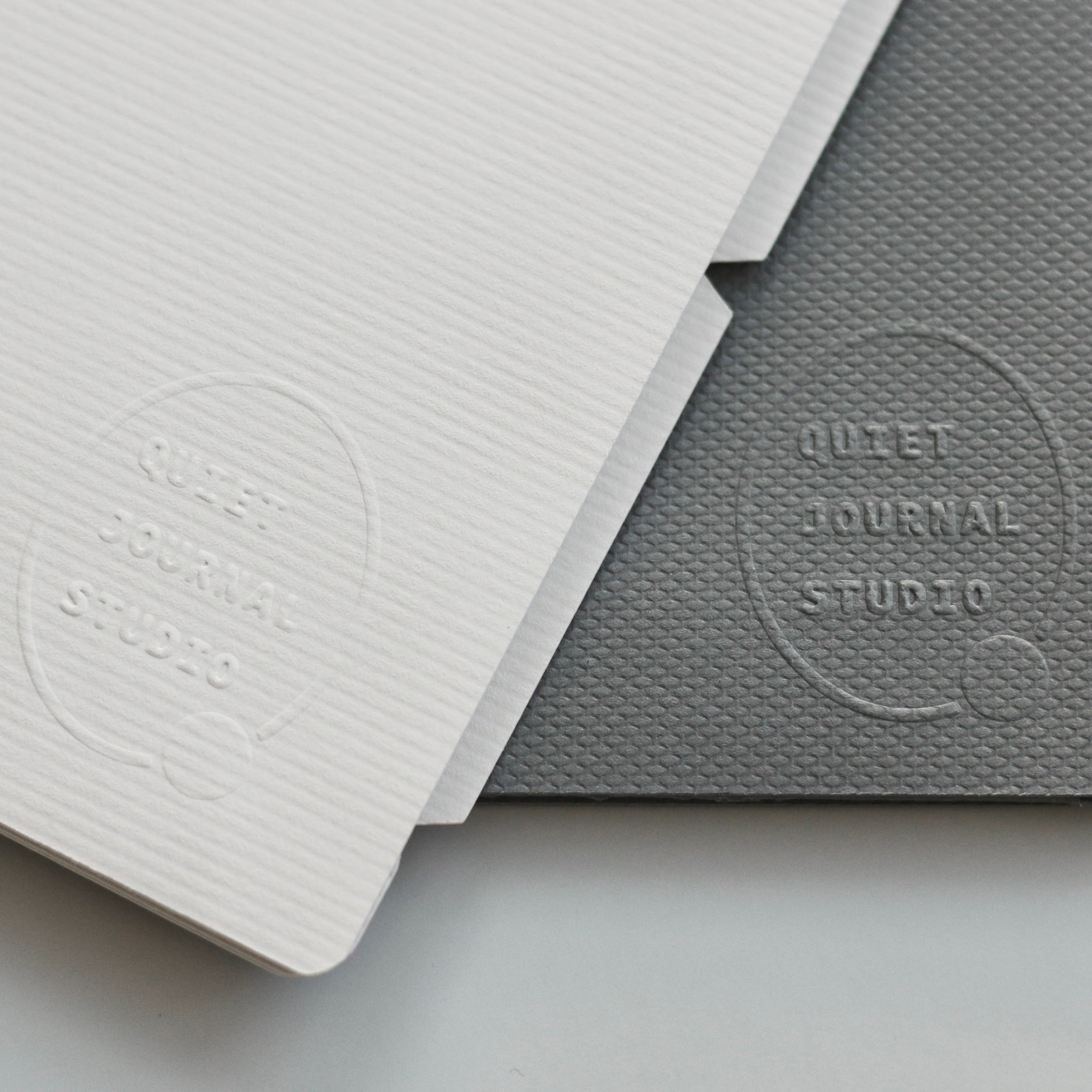 Two dividers, one light gray and one dark gray, with 'Quiet Journal Studio' embossed on them, on a light gray background.