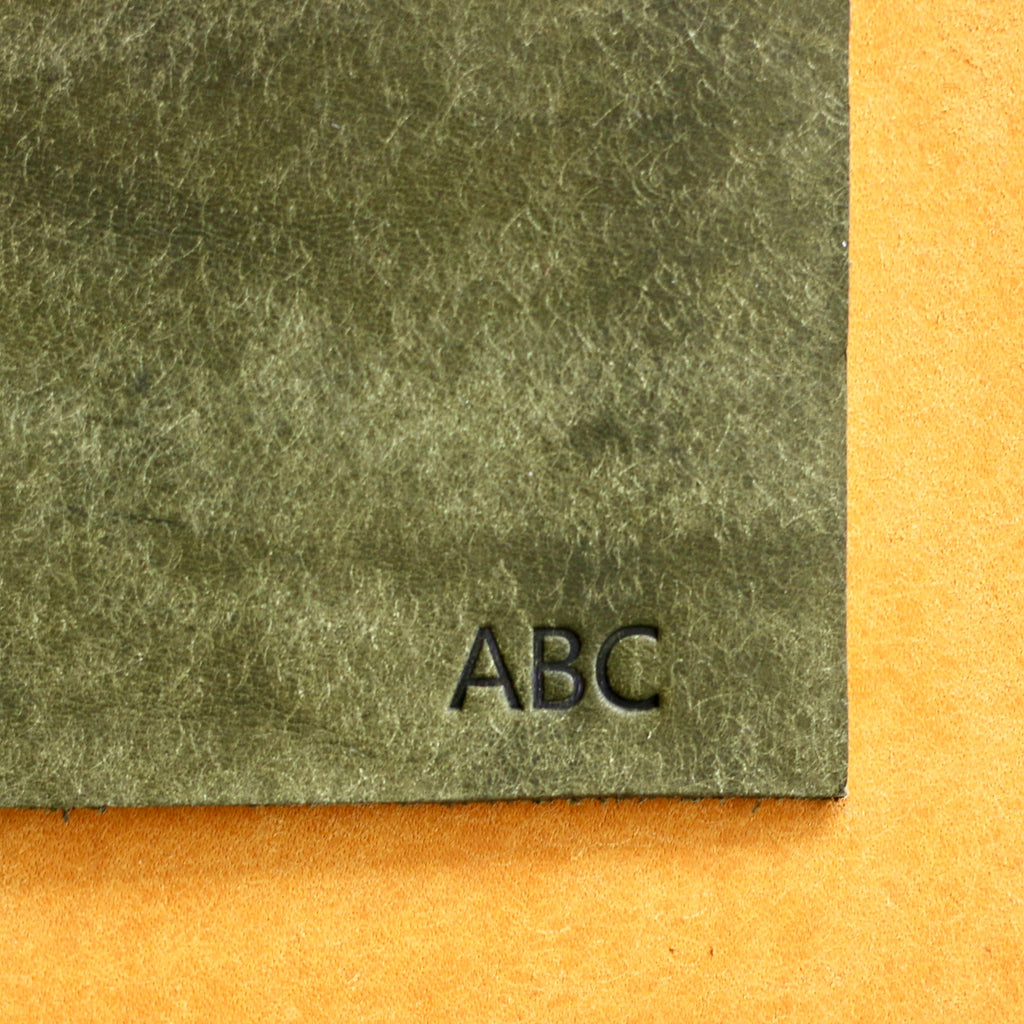 Two pieces of textured paper, one green and one orange, with 'ABC' embossed on the green piece.