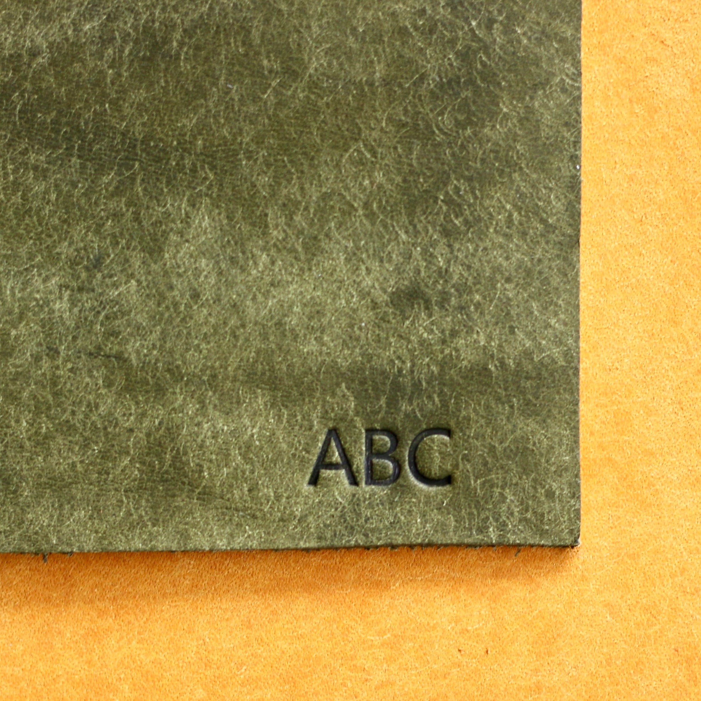 Two pieces of textured paper, one green and one orange, with 'ABC' embossed on the green piece.