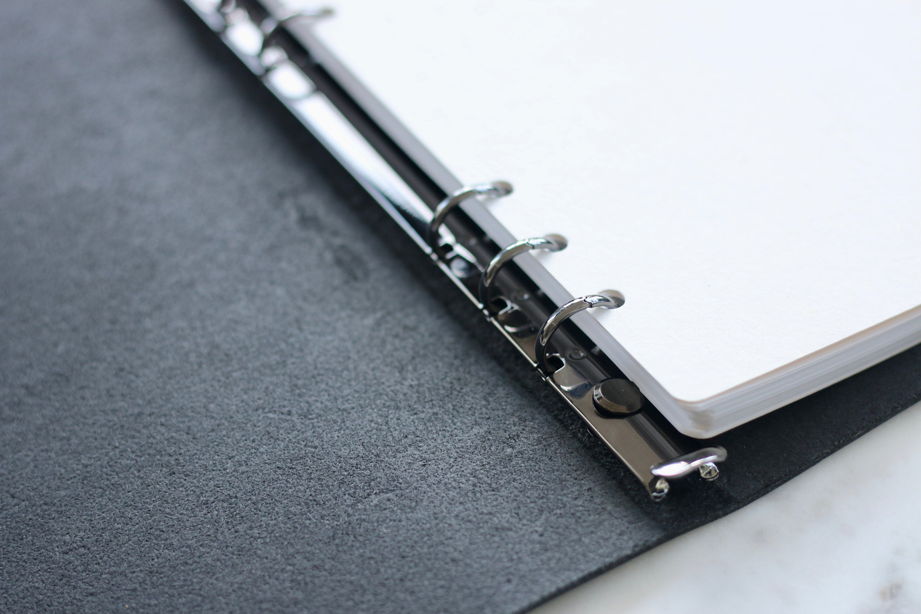 Close-up of a black notebook with a silver ring binder on a marble surface.