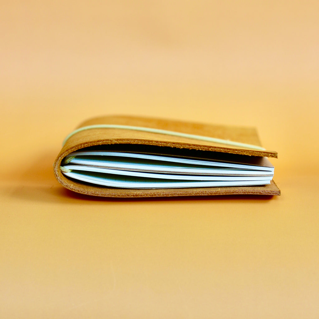Side of the leather journal with visible journals inside on a beige background