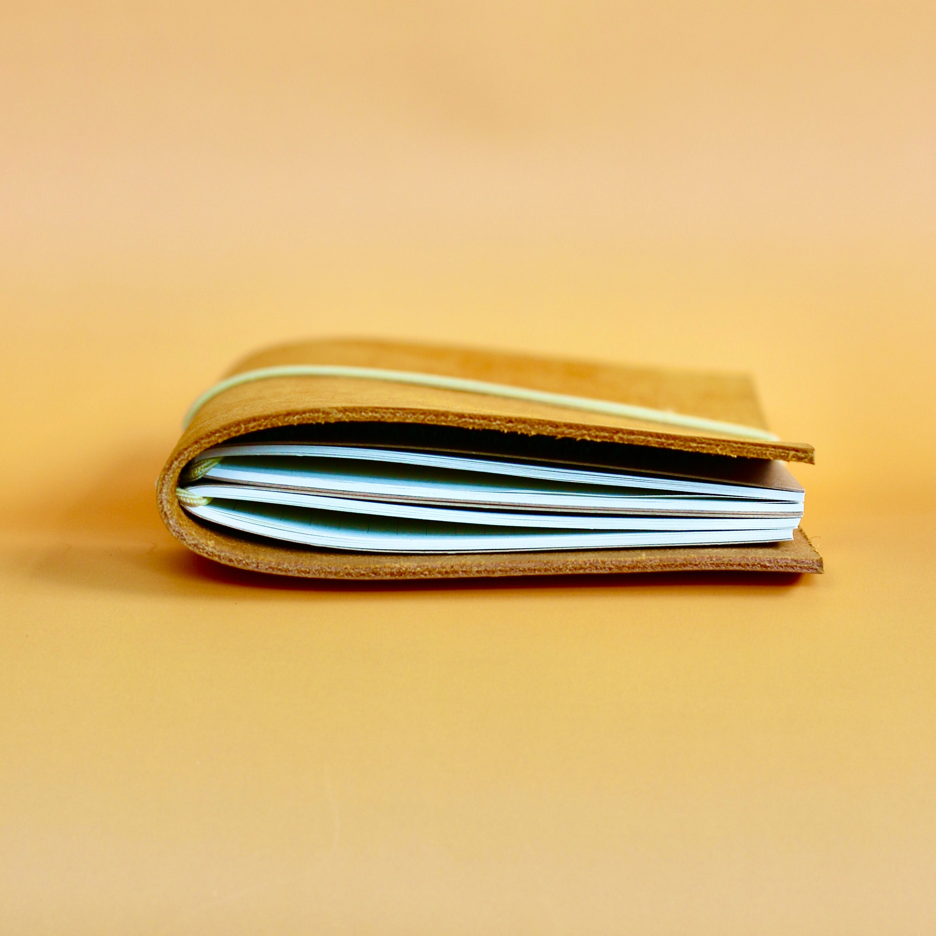 Side of the leather journal with visible journals inside on a beige background