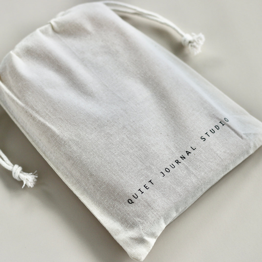 Beige drawstring bag with 'Quiet Journal Studio' text on a light gray background