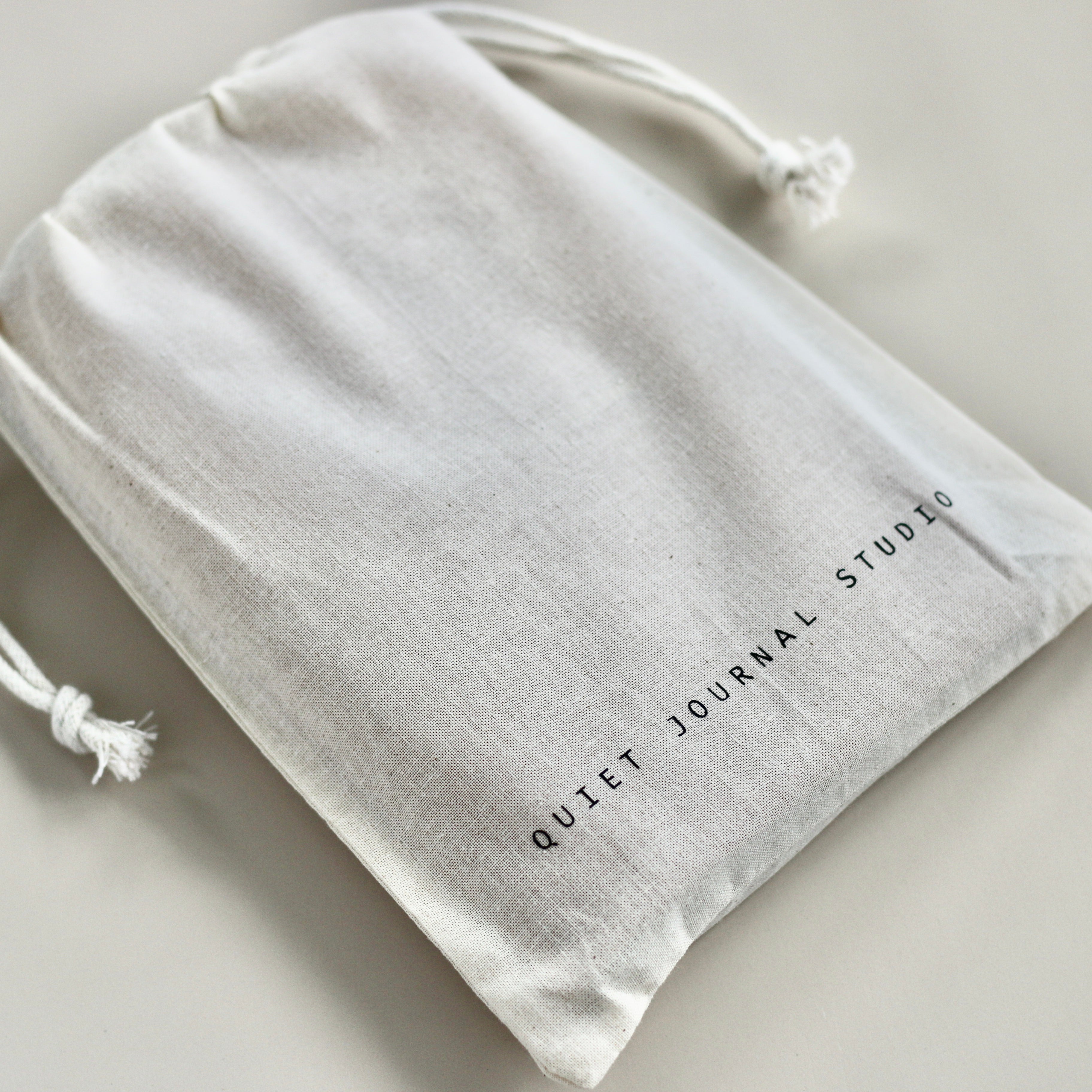 Beige drawstring bag with 'Quiet Journal Studio' text on a light gray background