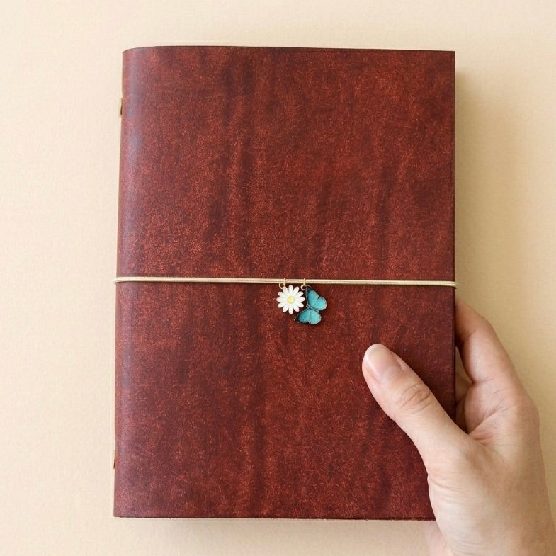 Red leather journal with two decorative charms held by a hand on a beige background
