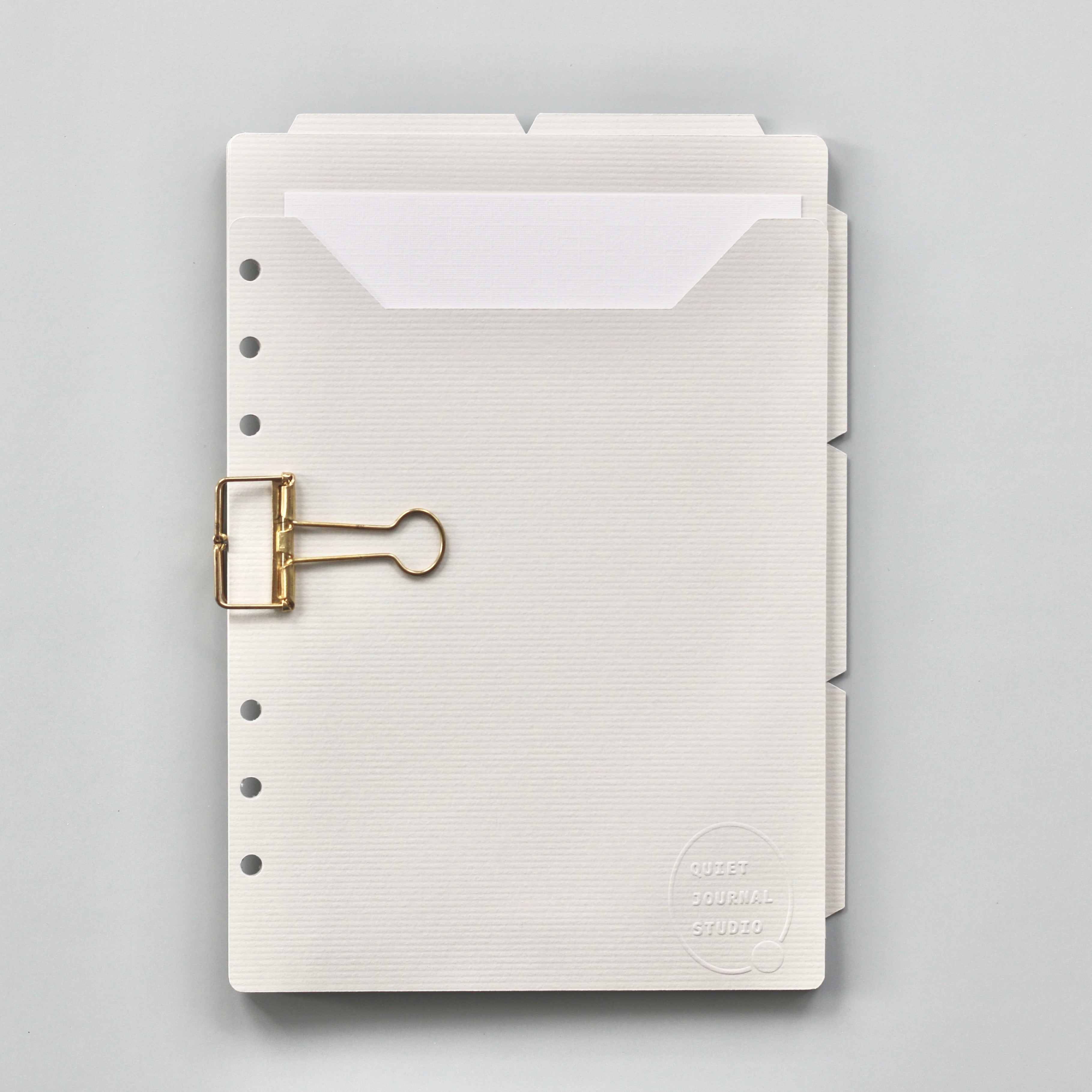 Light gray planner dividers with a gold clip on a gray background