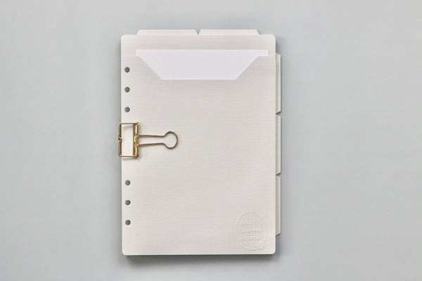 White planner with a gold clip on a gray background
